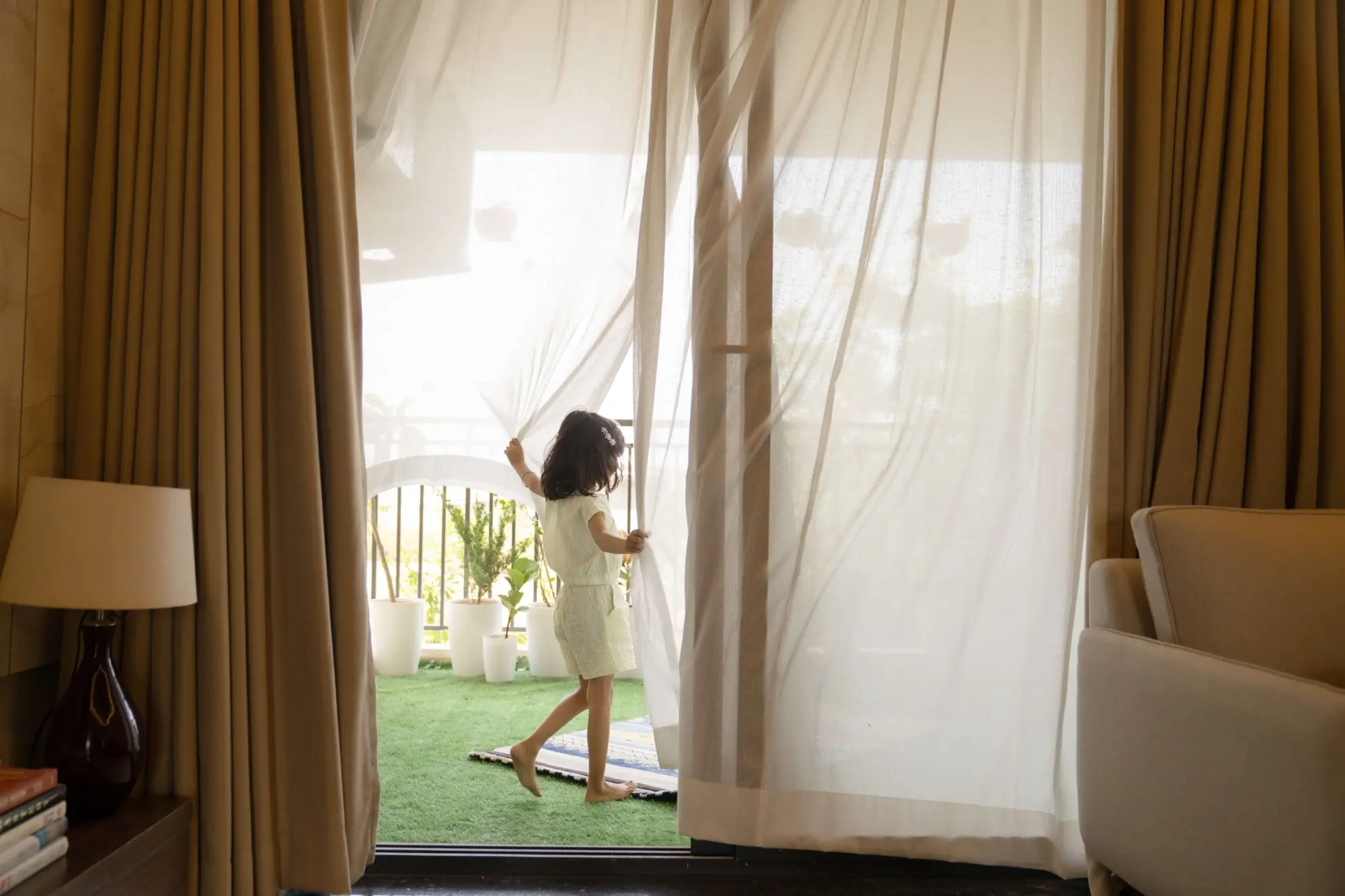 A girl drawing back sheer curtains to the balcony